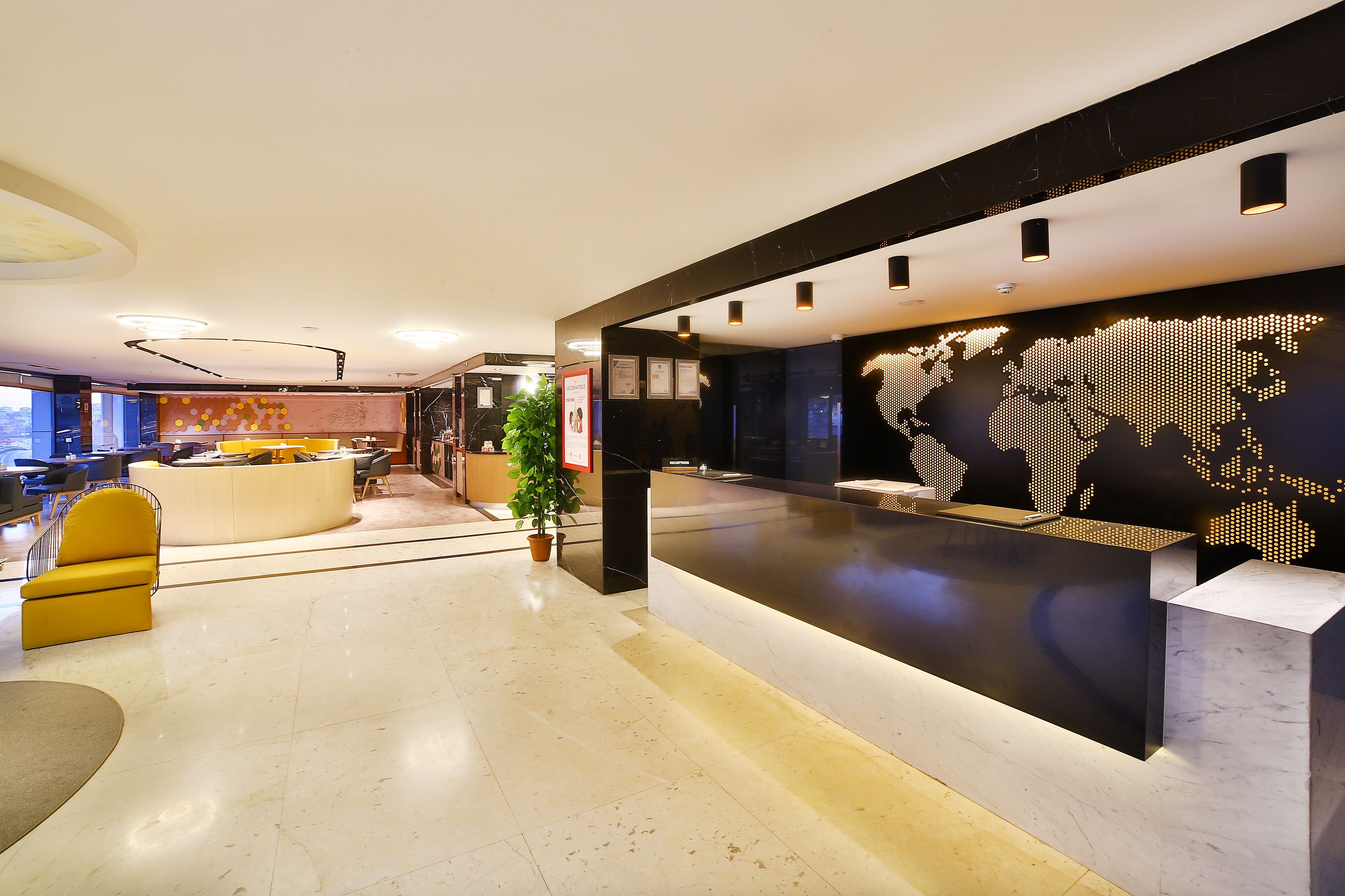 A modern reception area with a marble floor, a reception desk, a world map mural, and a yellow armchair.