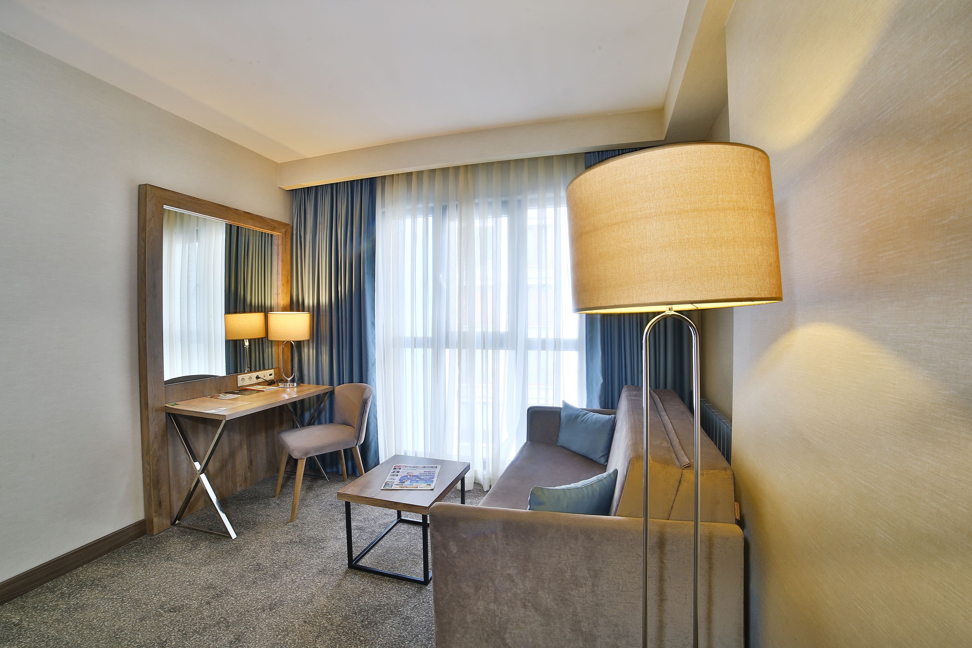 Habitación de hotel con escritorio, silla, sofá y una lámpara grande.