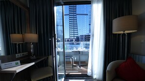 A hotel room with a desk, two lamps, a red pillow, a sofa, and a city view through a glass door. - ibis Styles Istanbul Bomonti (Istanbul)