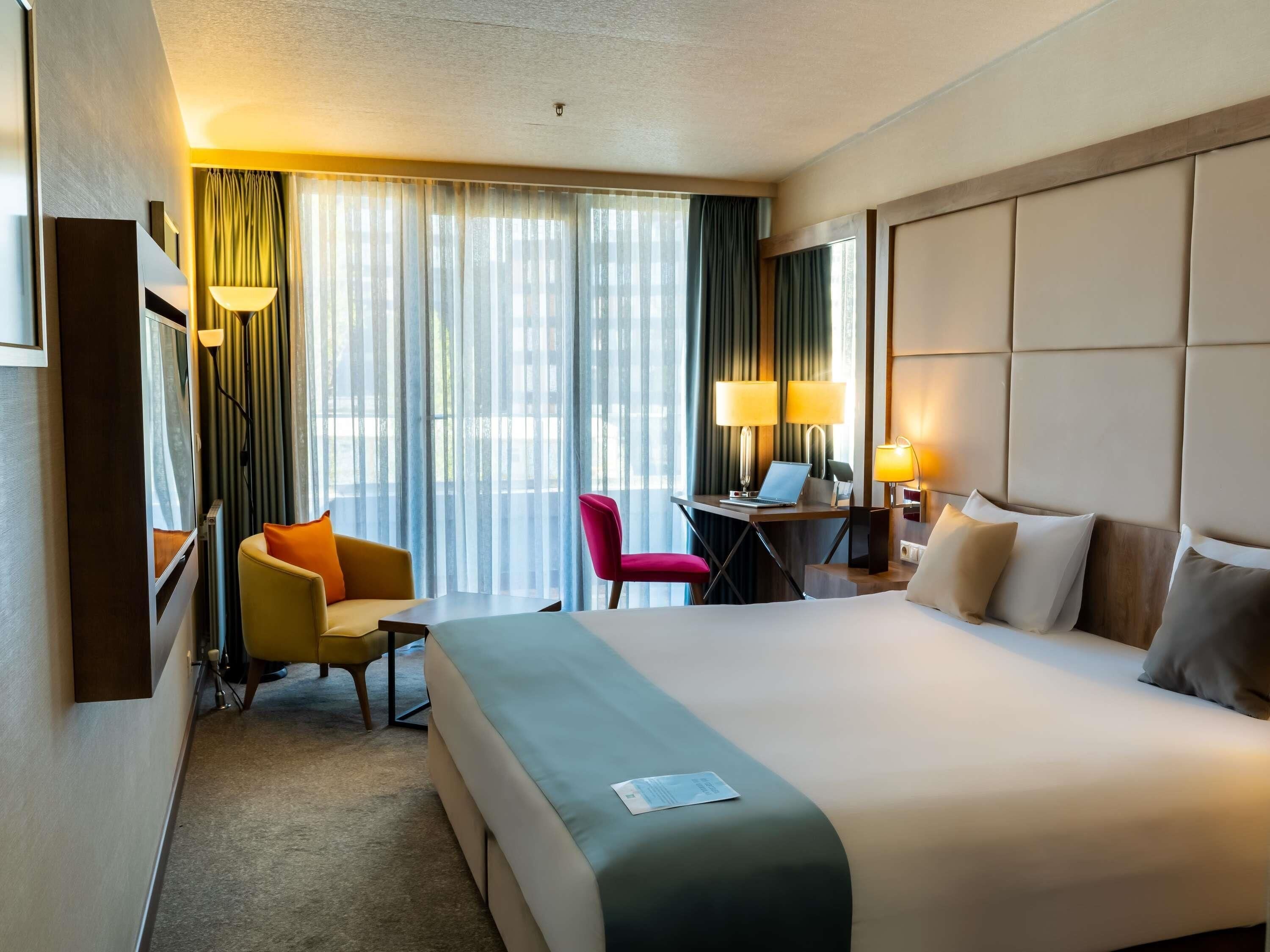 Une chambre d’hôtel avec un grand lit, un bureau avec un ordinateur portable, une chaise et une lampe de bureau.