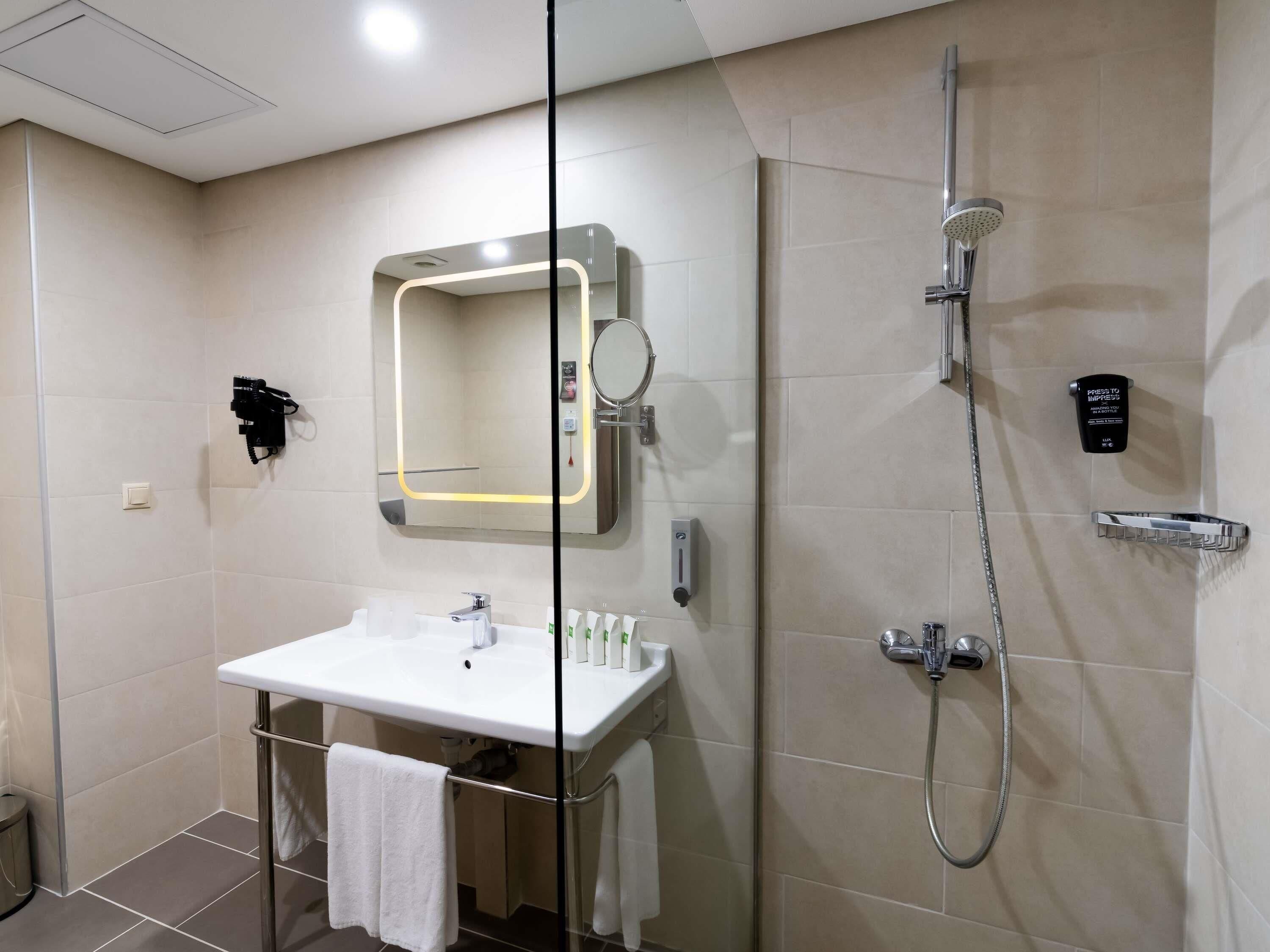 A modern bathroom with a glass partition, a white sink, a handheld showerhead, and a towel rack.