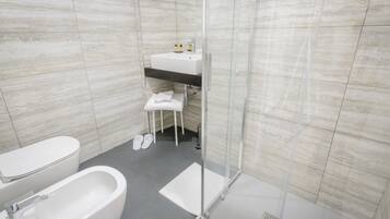Casa de banho moderna com sanita, bidé e cabine de duche envidraçada.