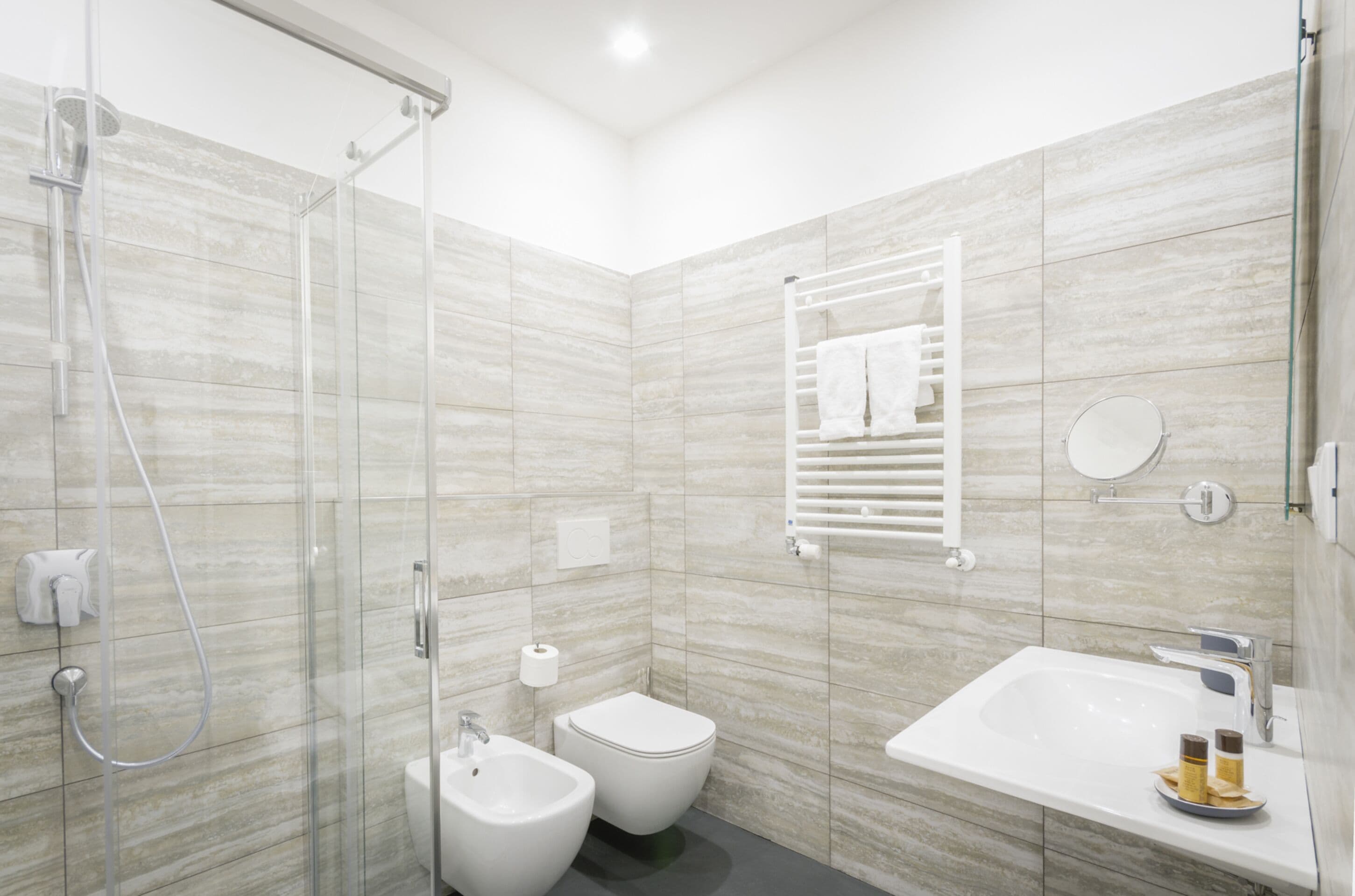 Un baño moderno con cabina de ducha de vidrio, un bidé, un inodoro y un lavamanos con espejo.
