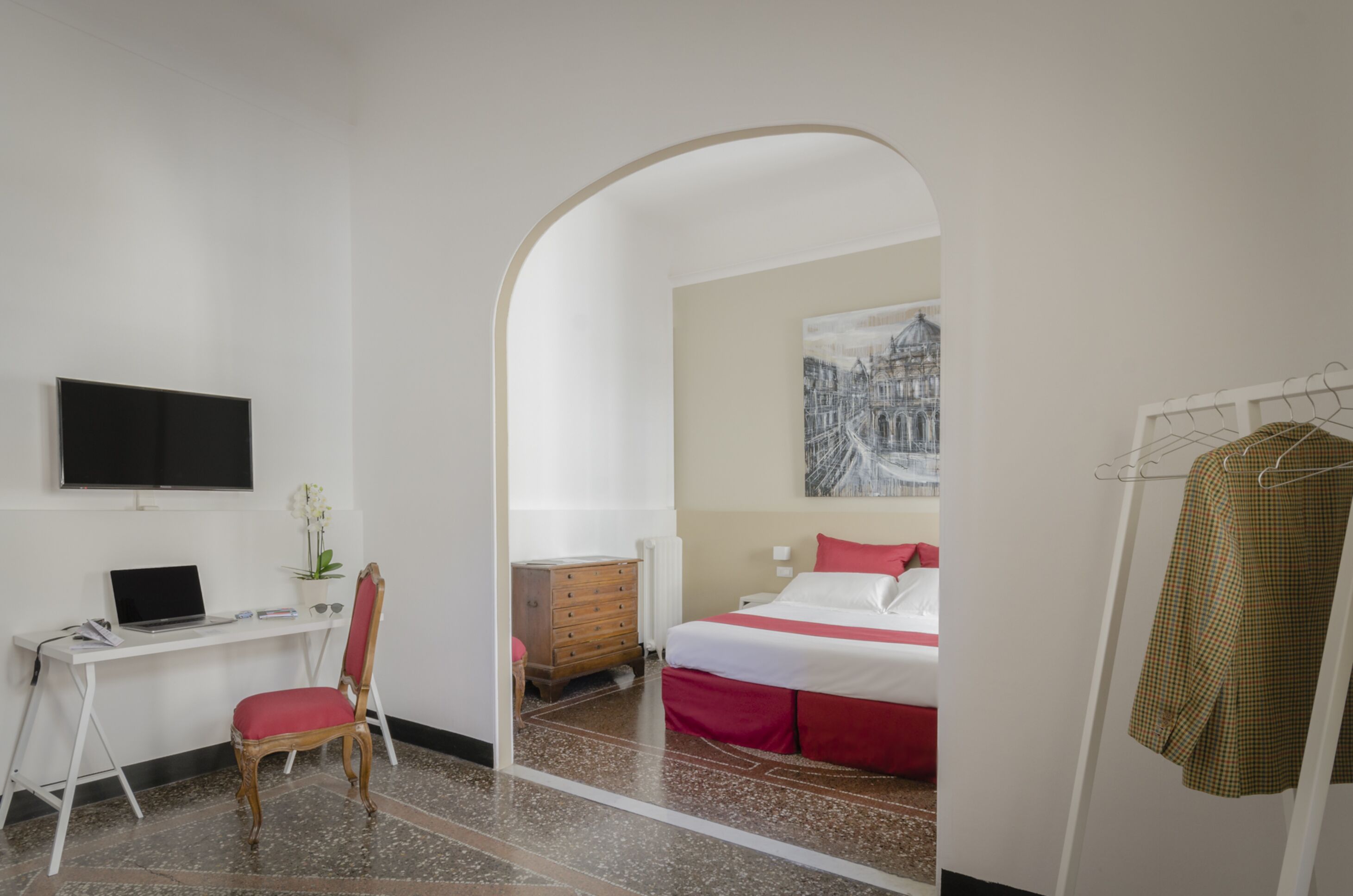 A hotel room with a desk, chair, bed, and a painting on the wall.