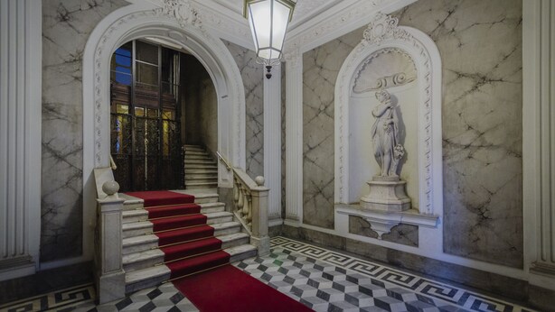 A grand staircase with a red carpet, marble walls, and a statue. - Genova46 Suites & Rooms (Genoa)