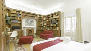 A hotel room with a large bed, a fireplace, a bookshelf, and a desk with a chair. - Genova46 Suites & Rooms (Genoa)