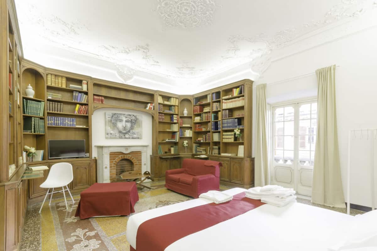 A hotel room with a large bed, a fireplace, a bookshelf, and a desk with a chair.