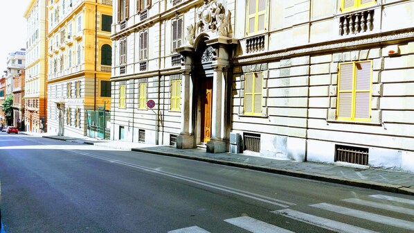 A street view with a building featuring classical architecture, including columns and decorative elements.