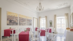 A dining area with white tables and chairs, red tablecloths, and a chandelier. - Genova46 Suites & Rooms (Genoa)