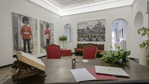 A conference room with a large table, red chairs, a bench, and paintings on the walls. - Genova46 Suites & Rooms (Genoa)