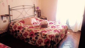 Een slaapkamer met een metalen bedframe, bloemenbeddengoed, een nachtkastje met een lamp en een wandplank.