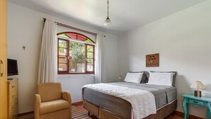 Un dormitorio con cama, una silla, un escritorio y una ventana con cortinas.