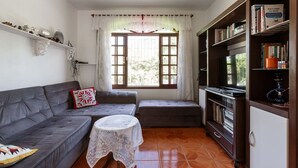 Una sala de estar con un sofá gris, una mesita redonda, una estantería y una ventana con cortinas.