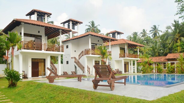 A resort with multiple white buildings, a swimming pool, and palm trees. - Nature Paradise Villas (Balapitiya)