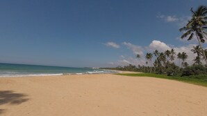 A wide sandy beach with gentle waves, palm trees, and a clear sky. - Nature Paradise Villas (Balapitiya)