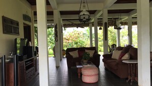 A covered outdoor living area with a sofa, ottoman, and television set. - Joglo Java (Semarang)