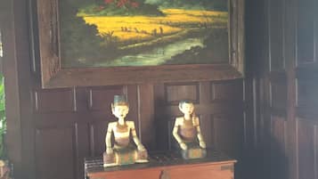 A painting of a landscape with a mountain and a river, two wooden sculptures, and a dark wooden cabinet.