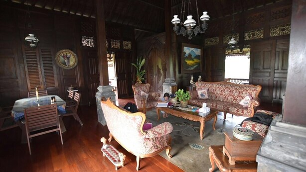 A traditional wooden interior with a dining area, a sofa set, and a chandelier. - Joglo Java (Semarang)
