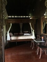 A traditional four-poster bed with white linens and a canopy, a wooden table with a chair, and a mirror on the wall.