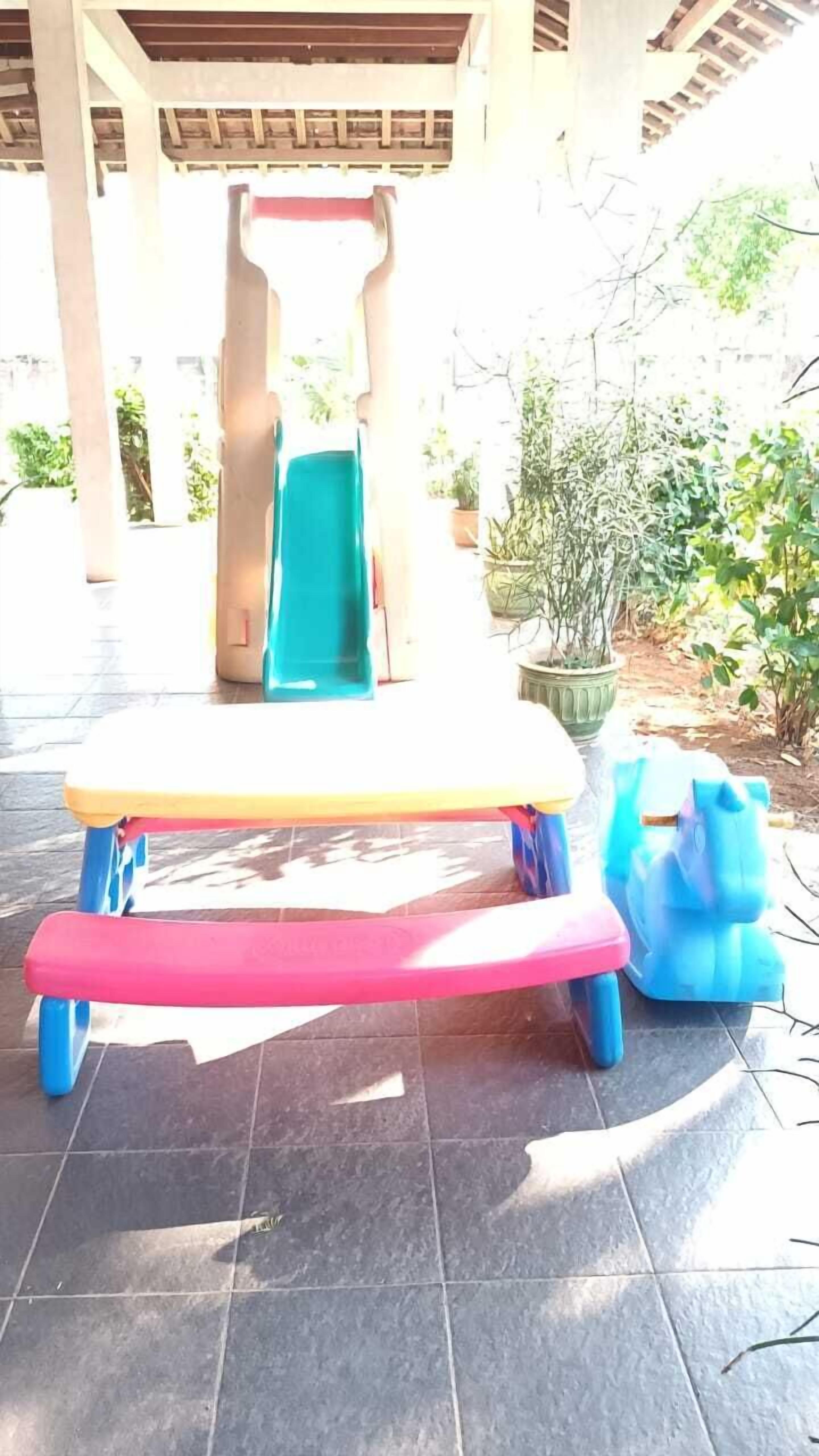 A children's play table with a slide, surrounded by potted plants and a tiled floor.