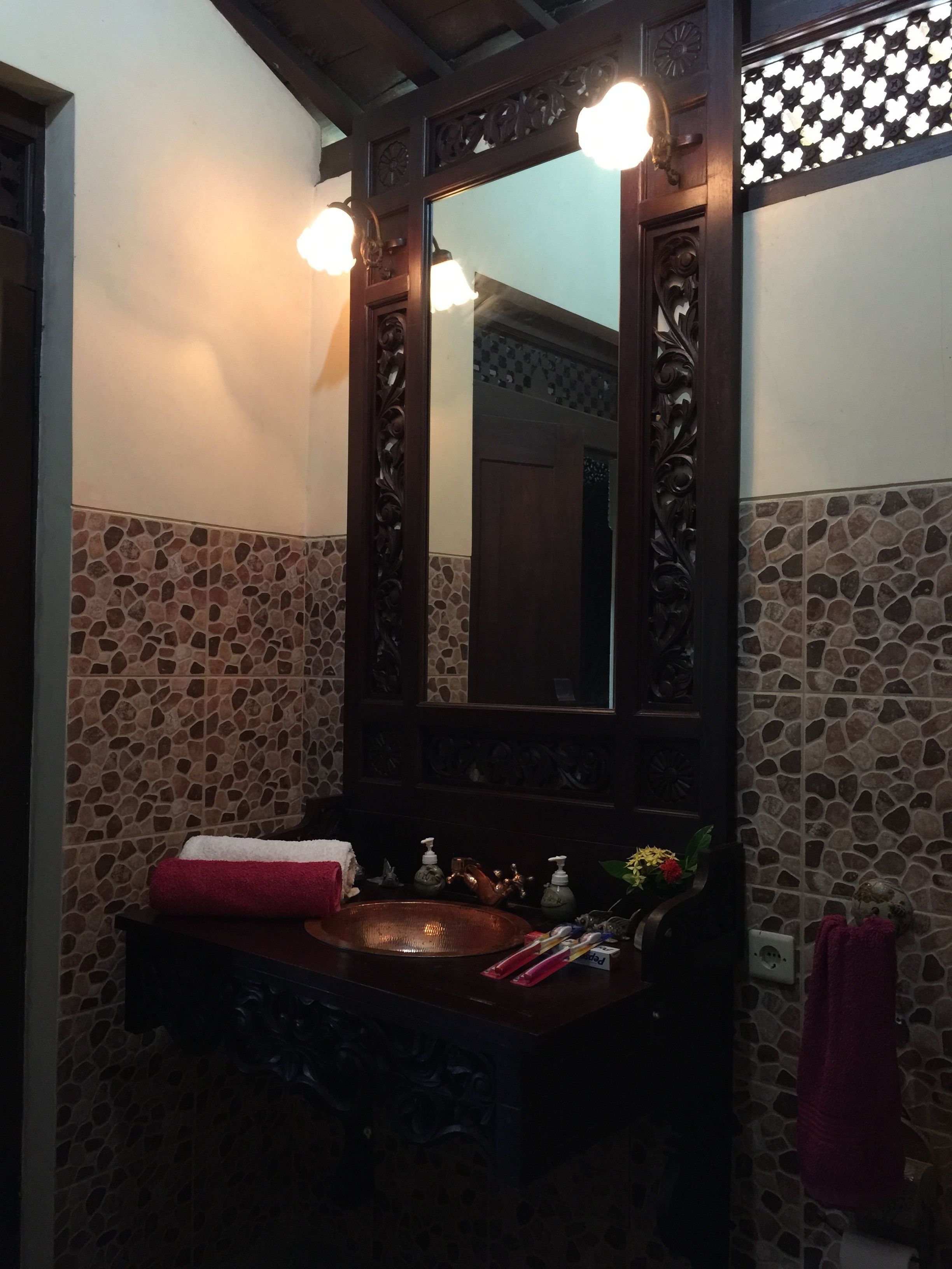 A bathroom with a stone-tiled wall, a wooden vanity with a copper sink, and a mirror with a wooden frame.