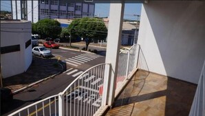A balcony with a metal railing overlooking a street with parked cars and a building in the background. - Roda Viva Park Hotel (Jales)
