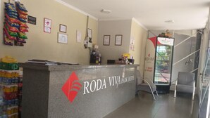 A reception desk at Roda Viva Park Hotel with a logo, a glass door leading to the lobby, and various items on the counter. - Roda Viva Park Hotel (Jales)