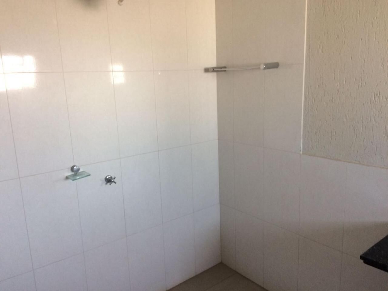 Um banheiro pequeno com azulejos, área de chuveiro, prateleira de vidro e porta-toalhas.