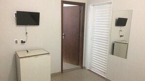 A room with a white refrigerator, a television mounted on the wall, a door with a mirror, and a window with blinds. - Roda Viva Park Hotel (Jales)