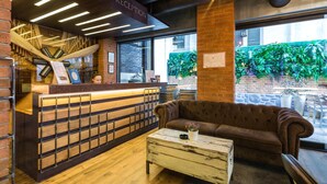 A reception area with a wooden desk, a brown sofa, and a white coffee table. There is a staircase with a wooden railing and a sign that reads "RECEPTION". - Passpartù (Belgrade)