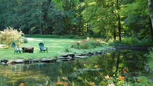 A serene garden with a pond, green chairs, and a wooden table.