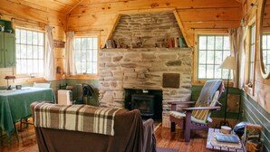 A cozy cabin interior with a stone fireplace, wooden walls, a dining area, and a comfortable seating area.