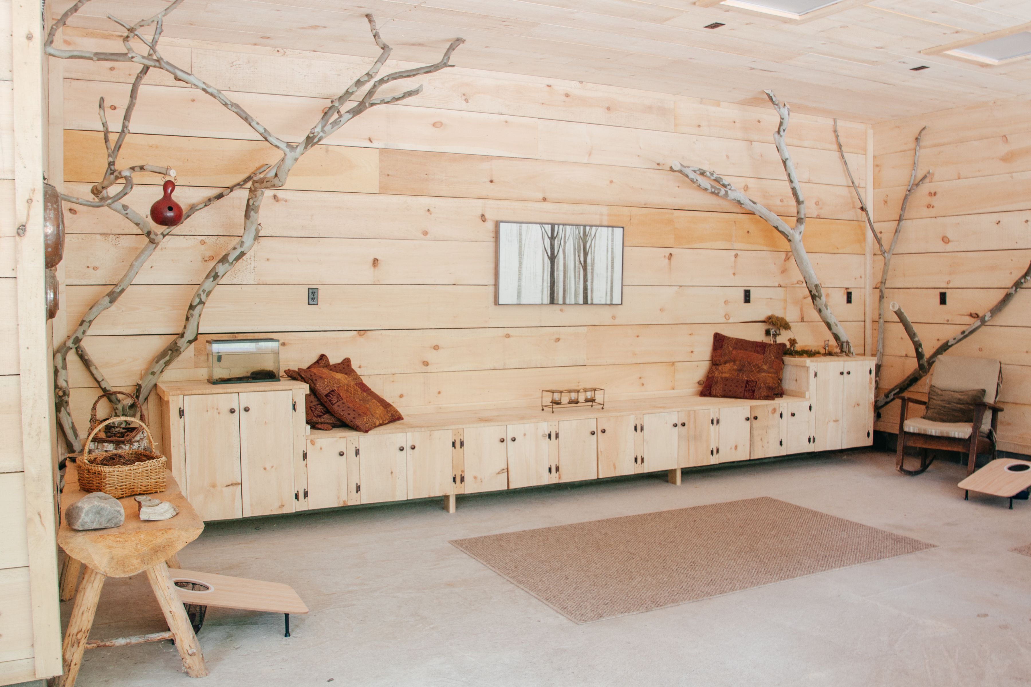 A cabin interior with a wooden bench, a small table with a basket, and a wall-mounted picture.