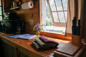 A wooden cabin interior with a wooden desk, a window with curtains, a vase with flowers, and a knife block. - Wellnesste Lodge and Cabin Rentals (Taberg)