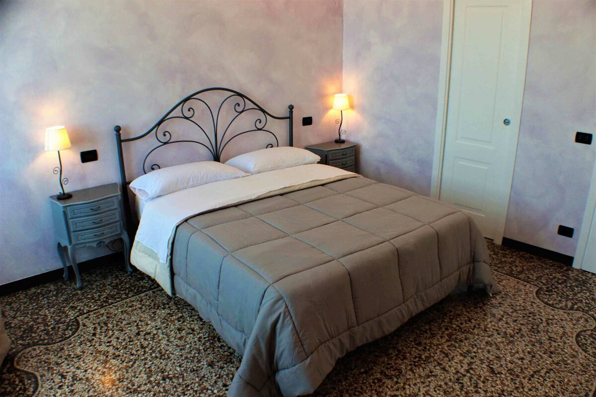 Una cama bien hecha con cabecera, dos mesitas de noche con lámparas y una puerta al fondo.