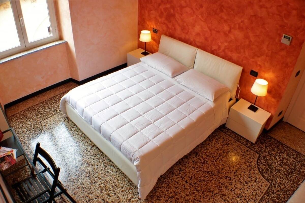 Una habitación de hotel con una cama grande, dos mesitas de noche con lámparas, una silla y una pequeña mesa con revistas.
