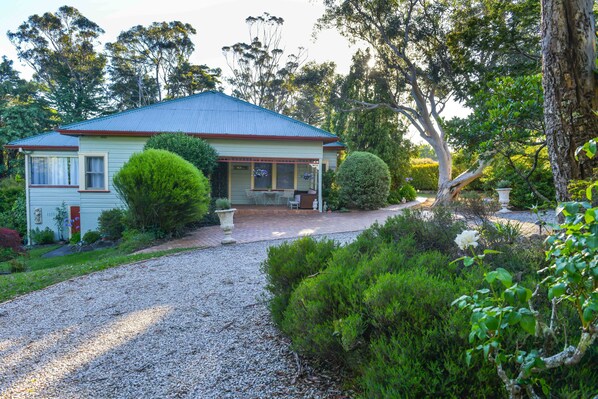 Situated in a lush environment, this charming house features a front porch with a bench and table.