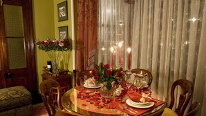 Uma sala de jantar com uma mesa redonda posta para quatro pessoas, rodeada por cadeiras de madeira com assentos acolchoados.