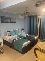 Un dormitorio con cama, mesitas de noche, una silla, ventilador de techo y ventana con cortinas.