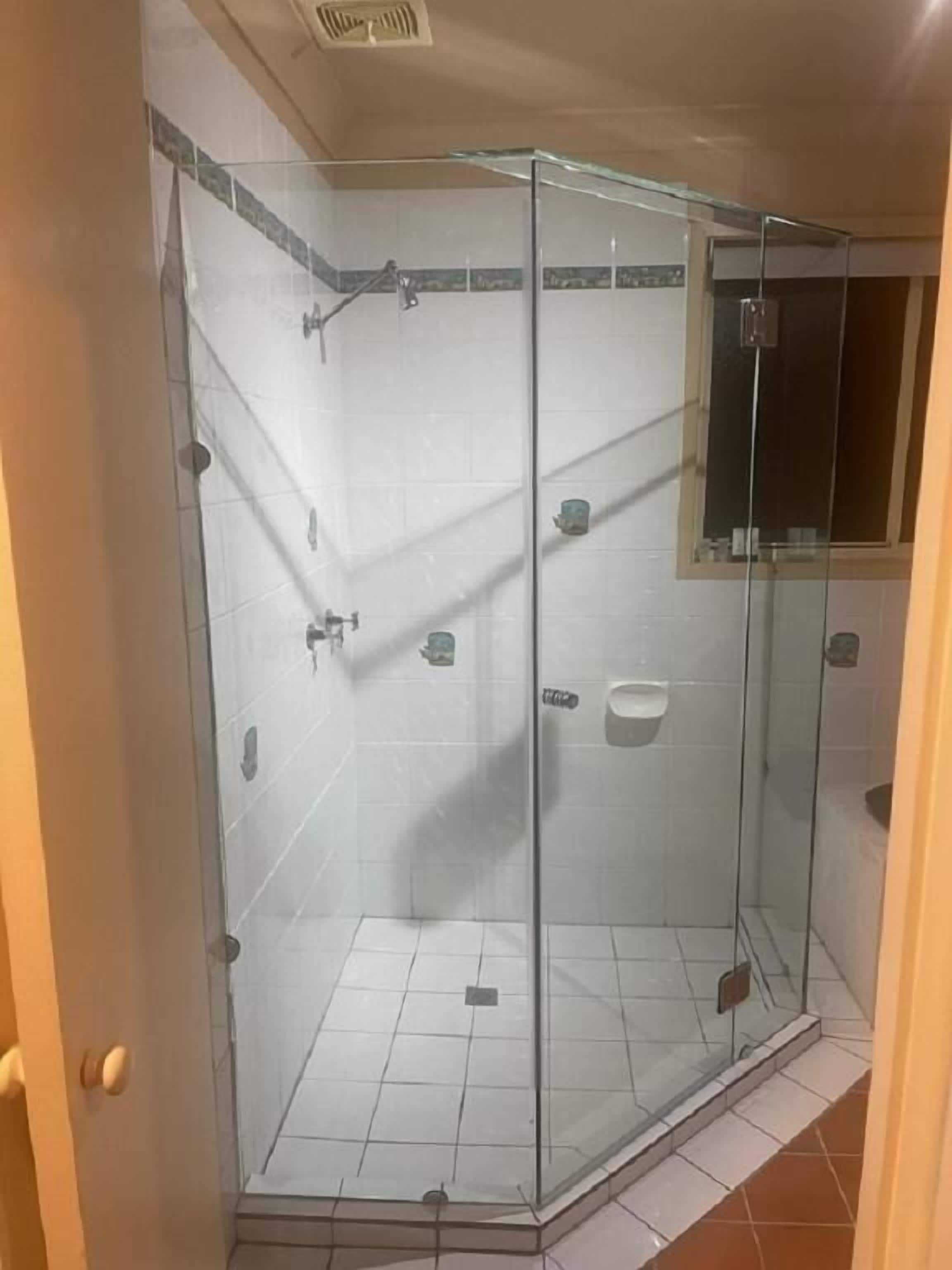 Et brusebad med glasvægge, flisegulv, brusehoved og sæbedispenser.