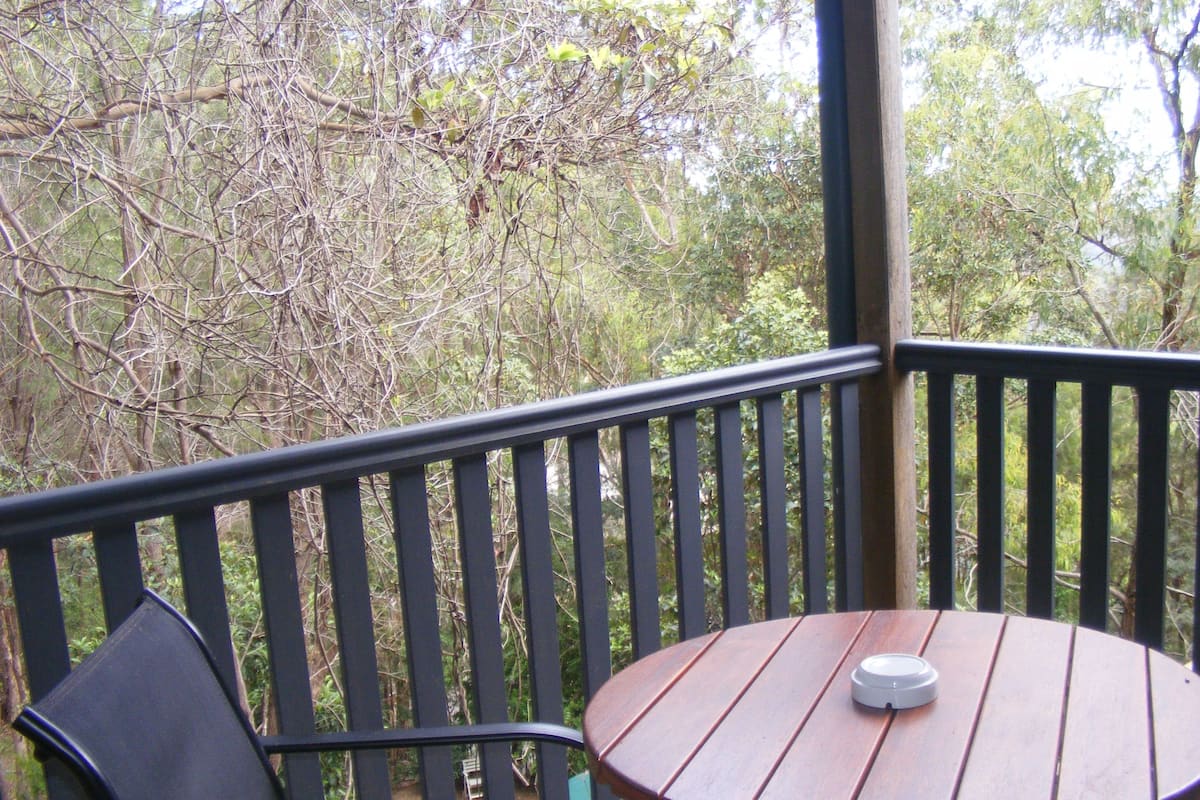 A wooden deck with a round table and a chair, surrounded by a black railing.