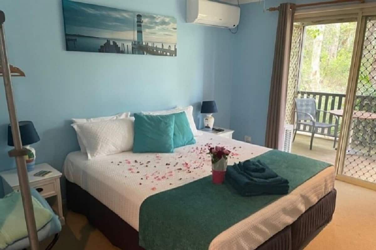 A bedroom with a bed, a nightstand, a chair, a window, and a balcony.