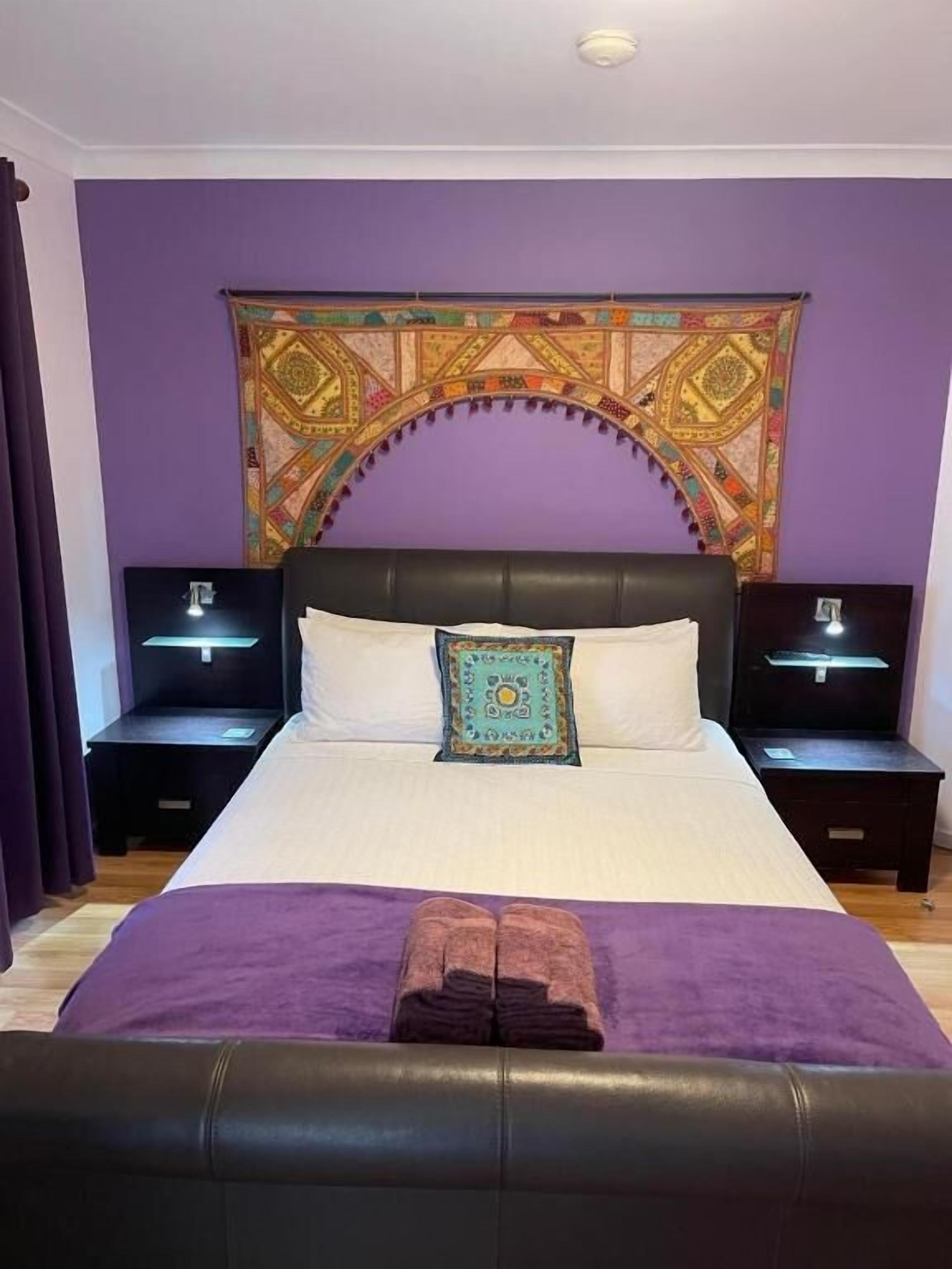 A bedroom with a large bed, two bedside tables, a tapestry, and a purple blanket.