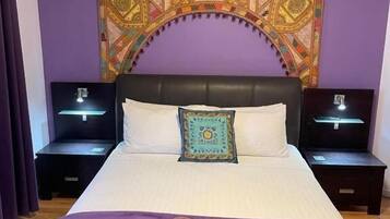 A bedroom with a large bed, two bedside tables, a tapestry, and a purple blanket.
