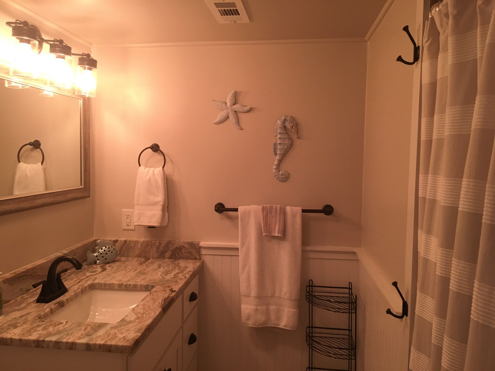 A bathroom with a marble sink, a mirror, a towel rack with towels, a seahorse decoration, and a shower curtain.