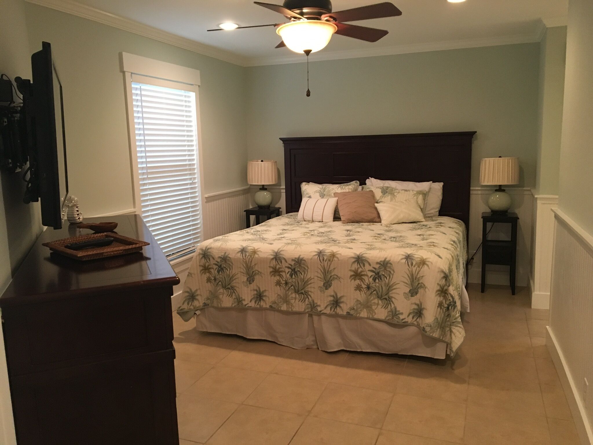 Une chambre à coucher comprenant un lit, deux tables de chevet avec des lampes, un ventilateur de plafond et une commode.