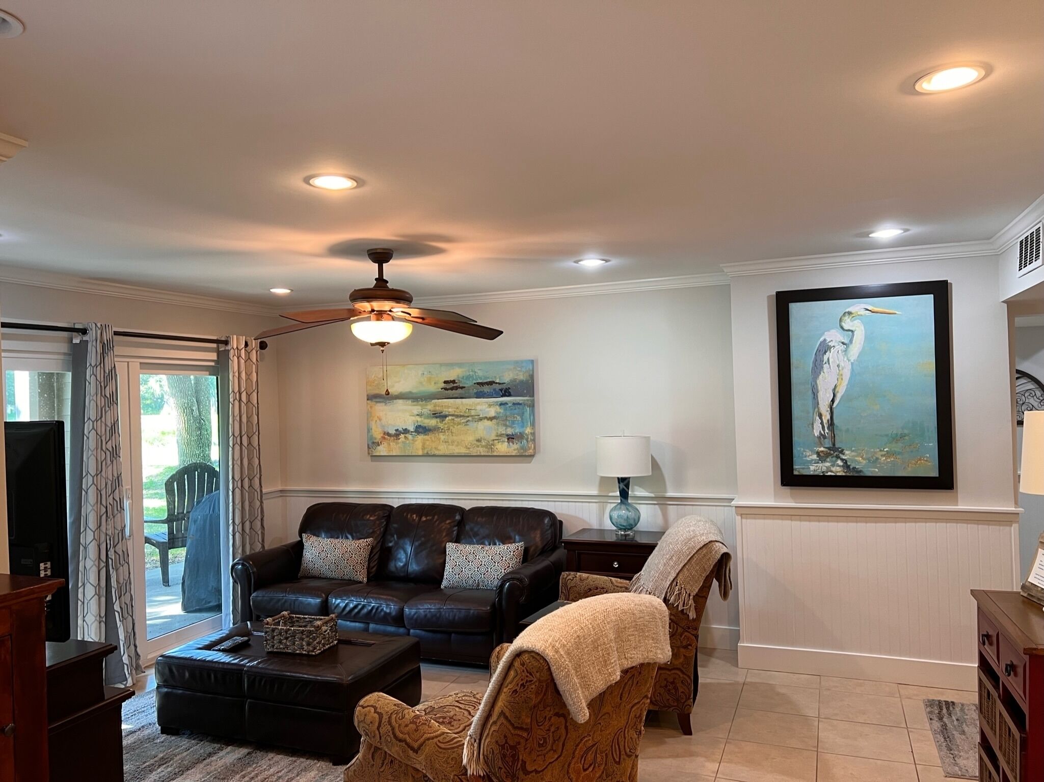 A living room with a dark leather sofa, a patterned armchair, a coffee table, and a painting of a bird.