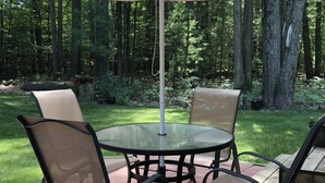 Et terrassemøbel med fire stole, en parasol og udsigt til et skovområde.