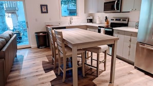 A modern kitchen with a wooden dining table, stainless steel appliances, and a view to the outside. - NEW 1 bedroom condo. This is the best location in Ketchum! (Ketchum)