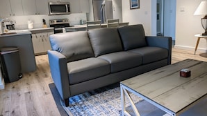 A modern kitchen with grey cabinets, a stainless steel refrigerator, and a microwave. There is a black leather sofa and a wooden coffee table in the living area. - NEW 1 bedroom condo. This is the best location in Ketchum! (Ketchum)